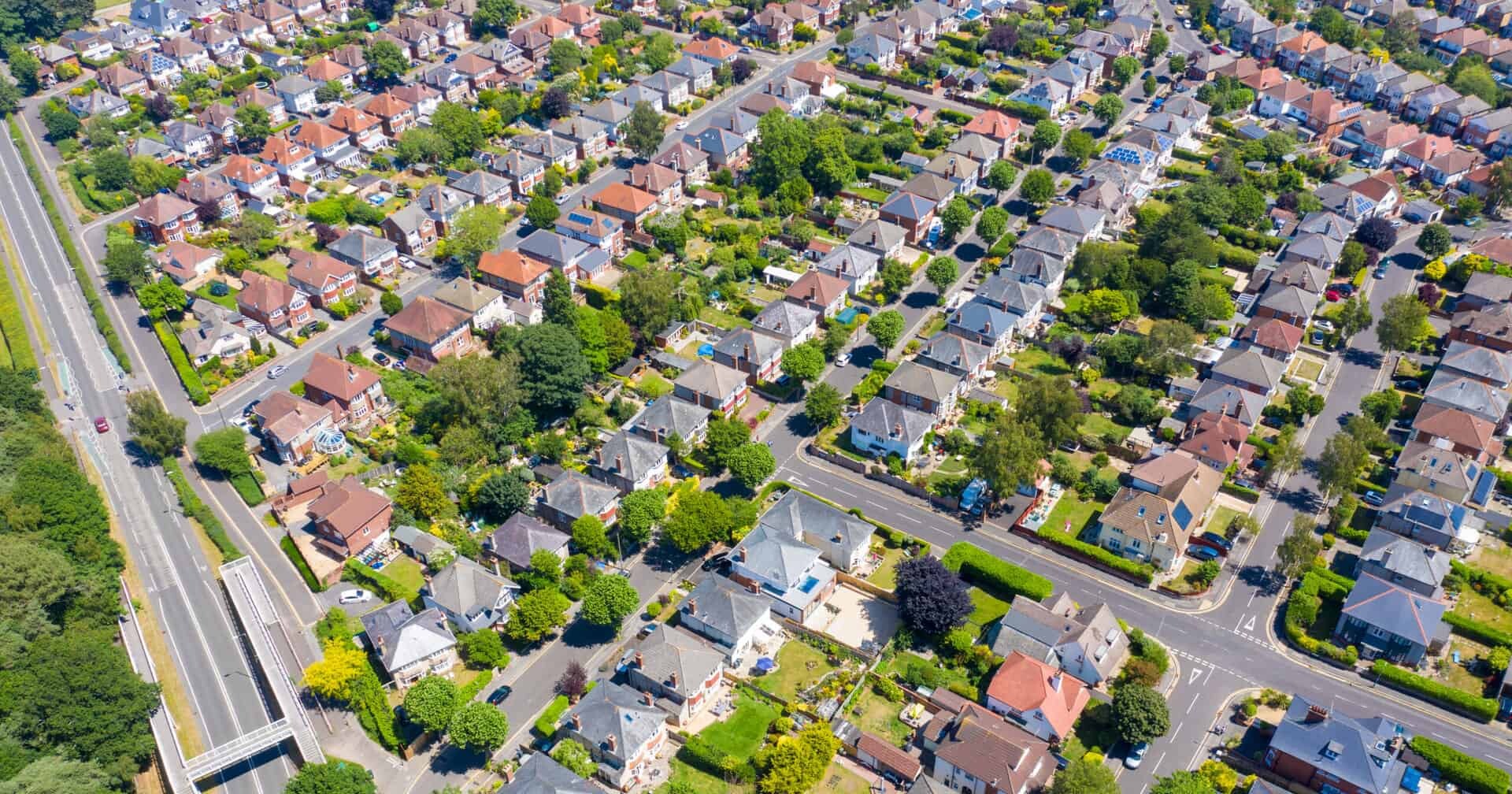 Bird's-eye view of detached houses in a leafy suburb on a sunny day.