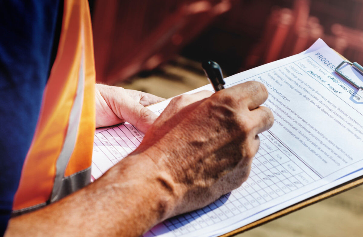 Close-up of a man wearing a builder's high-viz filling in a form on a clip board.