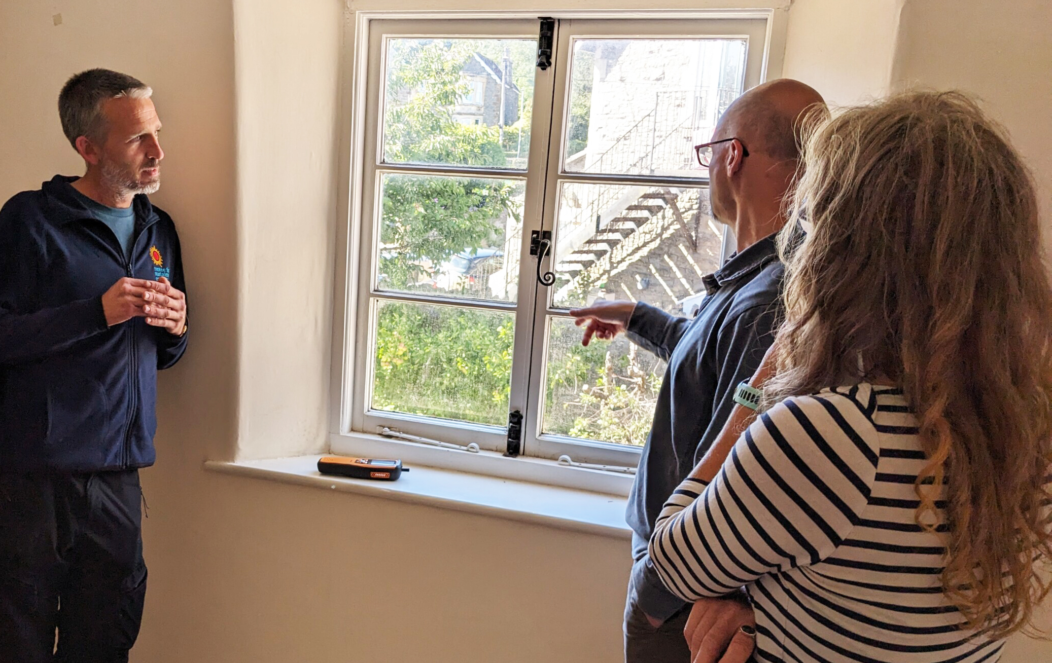 A surveyor in a branded fleece speaking to clients about making a window less draughty.