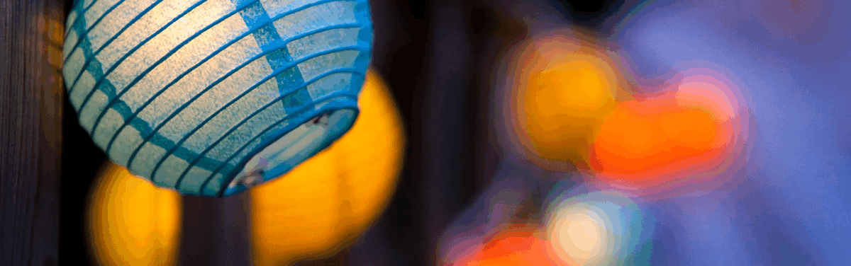 A teal lantern in focus with more yellow and orange lanterns blurred in the background