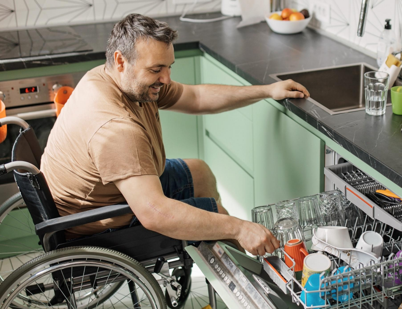 An independent wheelchair user empties a dishwasher in his kitchen.