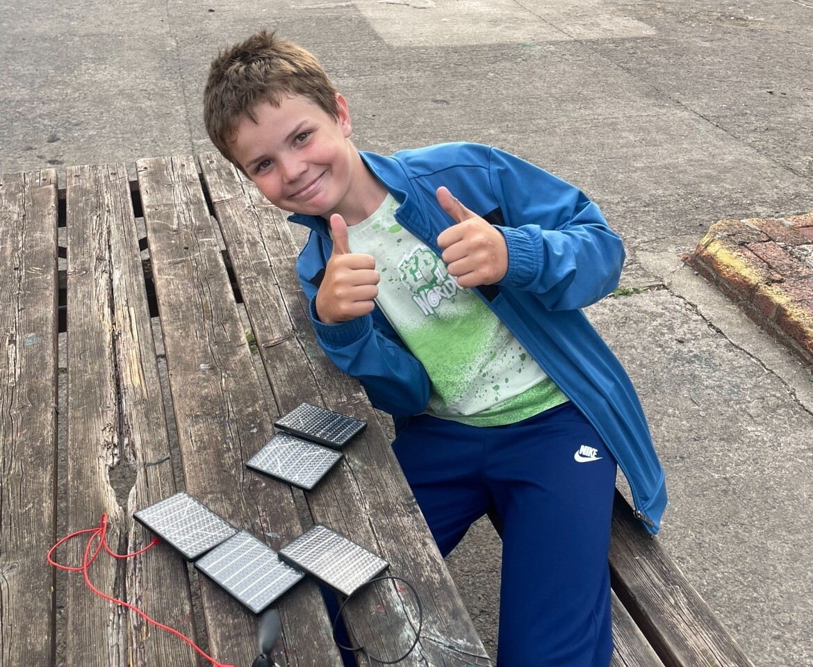 Boy smiling and giving thumbs up over mini solar panels and fan electronic system.