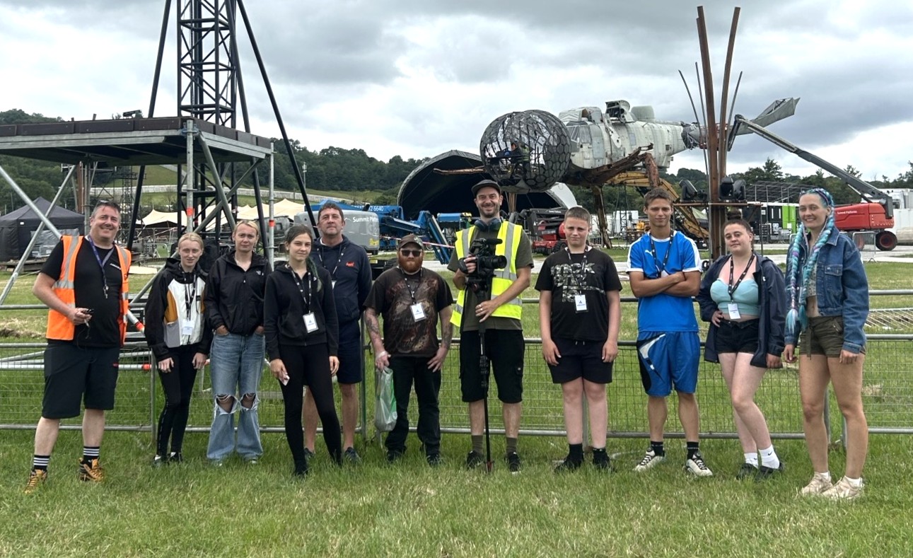 Young people standing in a field in front of a music stage.