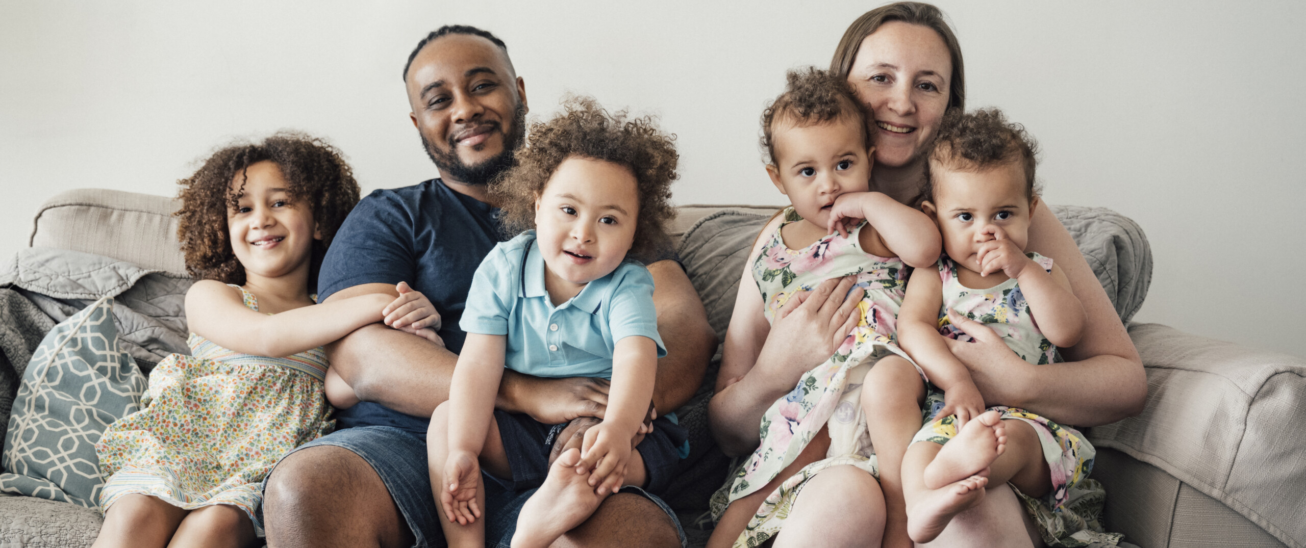 A diverse family sitting on a sofa smiling at the camera.