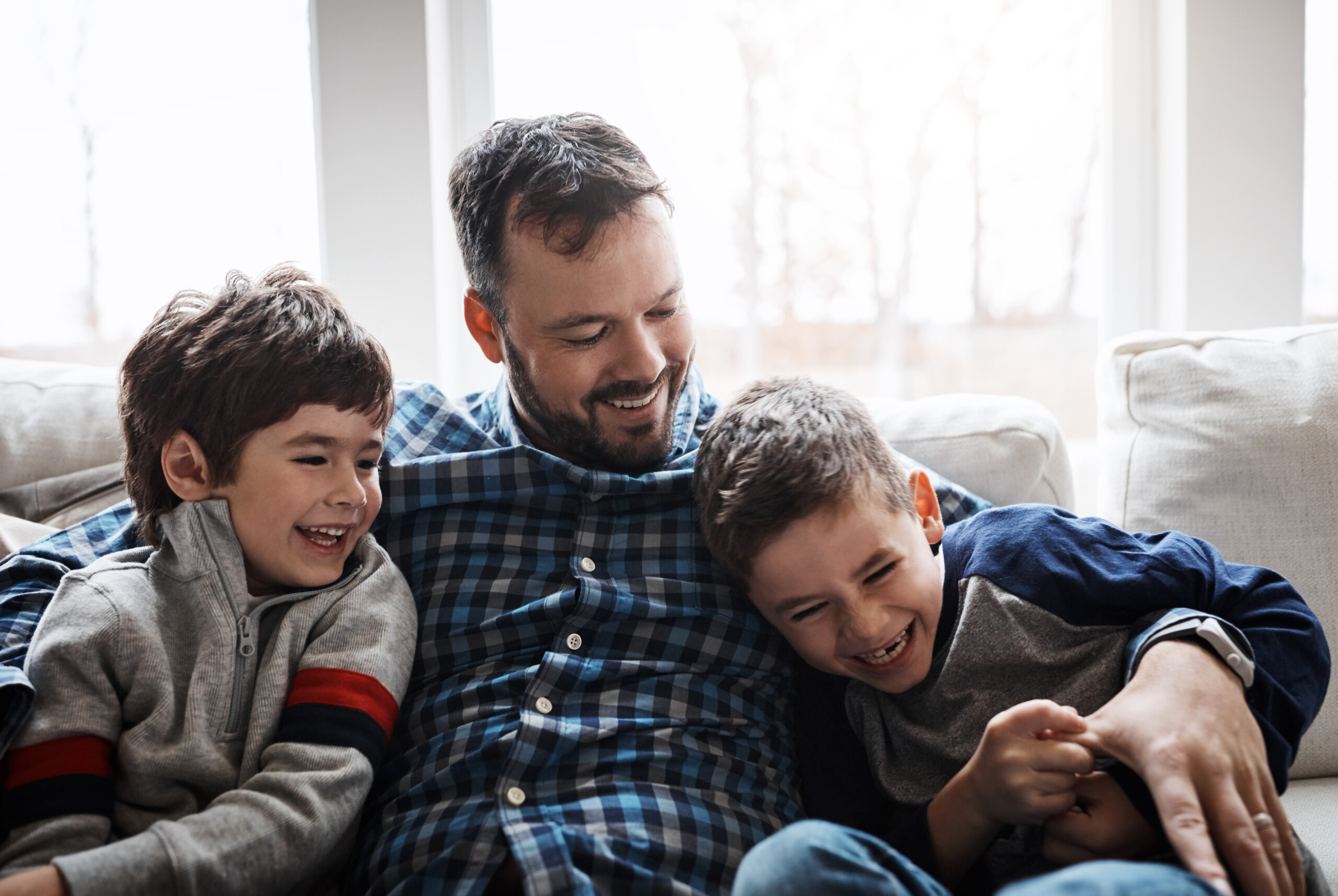 A father sitting on the sofa with his two sons, laughing.