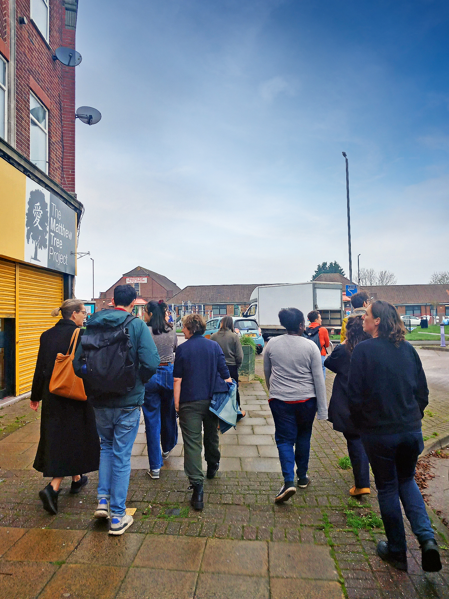 Group of people walking together on a residential street past The Matthew Tree Project building during a community walkabout