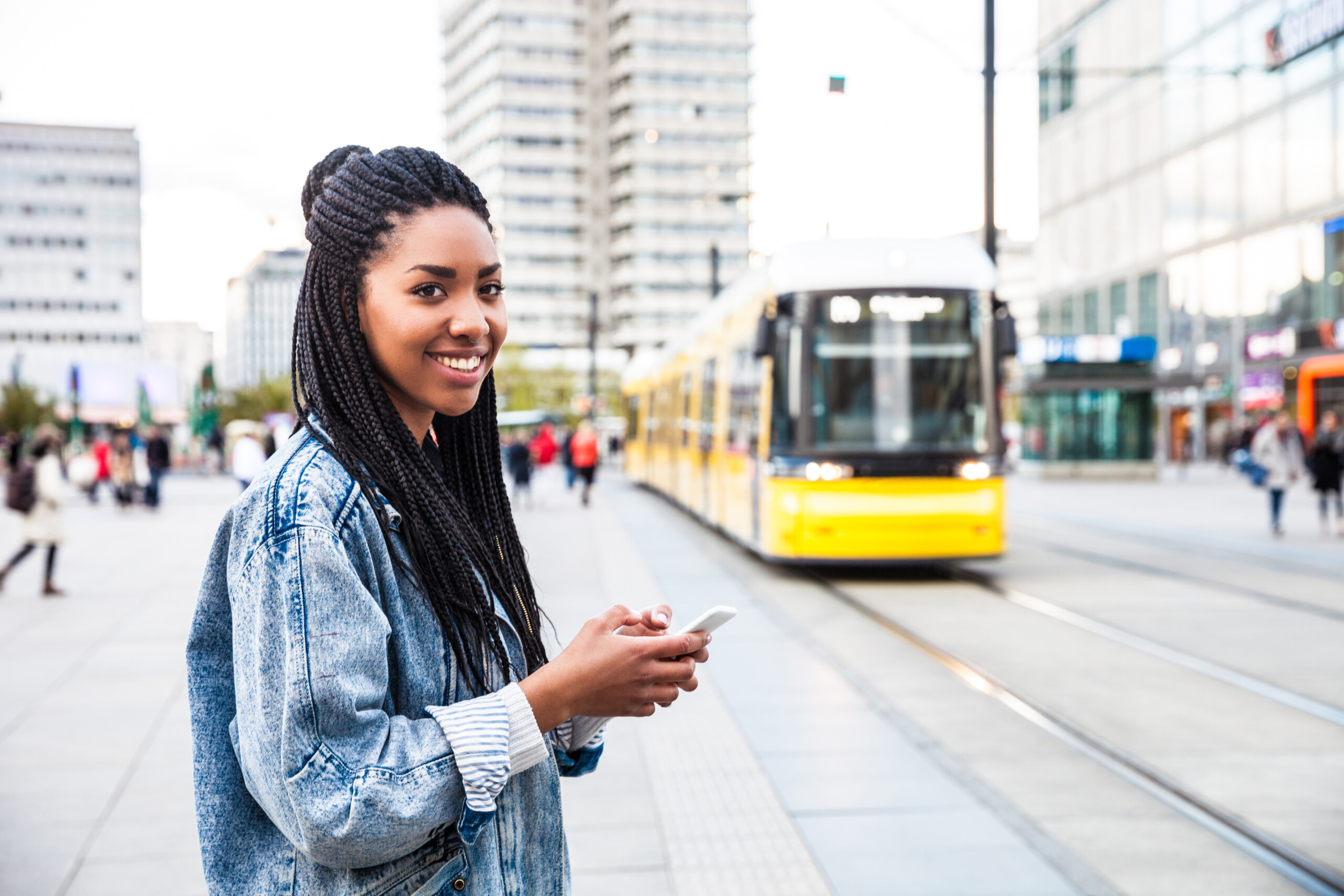Young woman standing beside busy street looking up from phone and smiling.