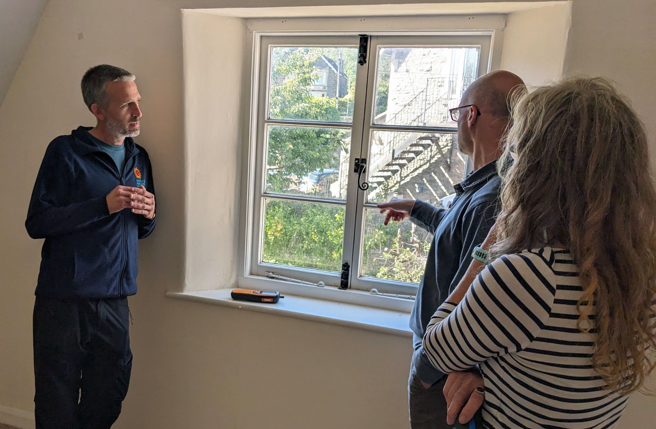 An energy advisor in branded fleece talks to home owners about a drafty window.