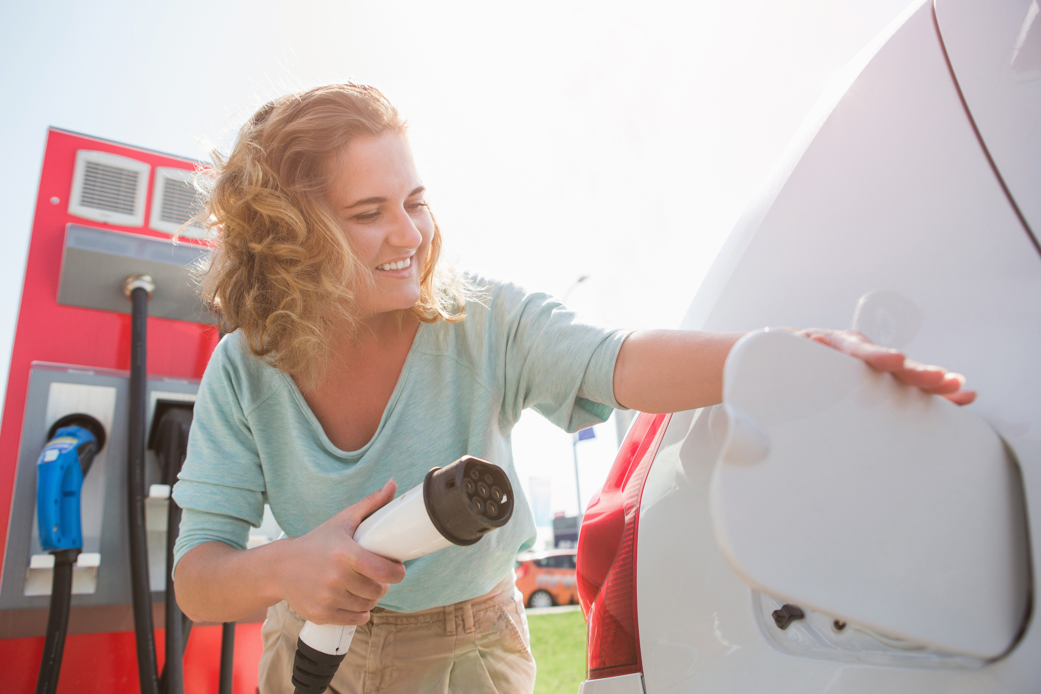 A smiling woman plugs in her electric car at a charging station