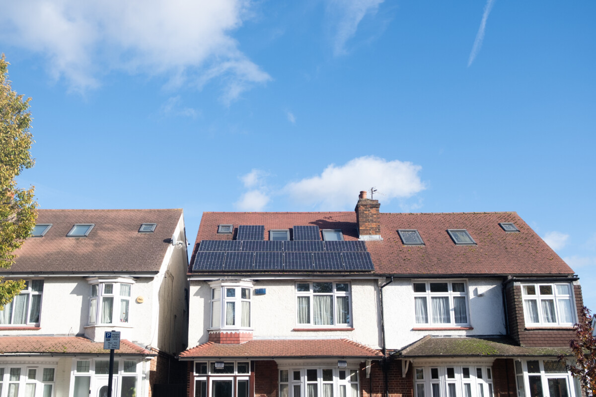 View of a row of British semi-detached homes under lots of blue sky. One house has solar panels on the roof.